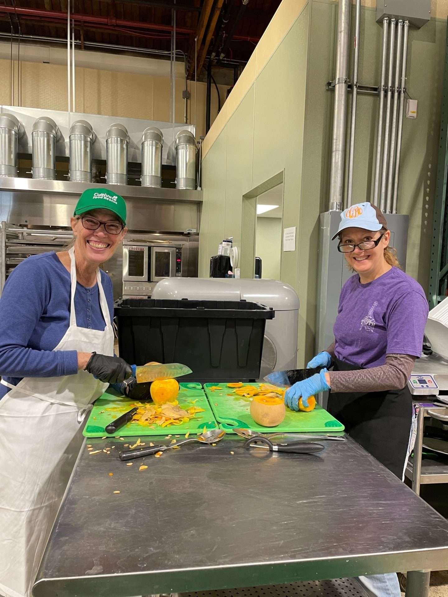 Two smiling volunteers slicing squash in the commercial food rescue kitchen
